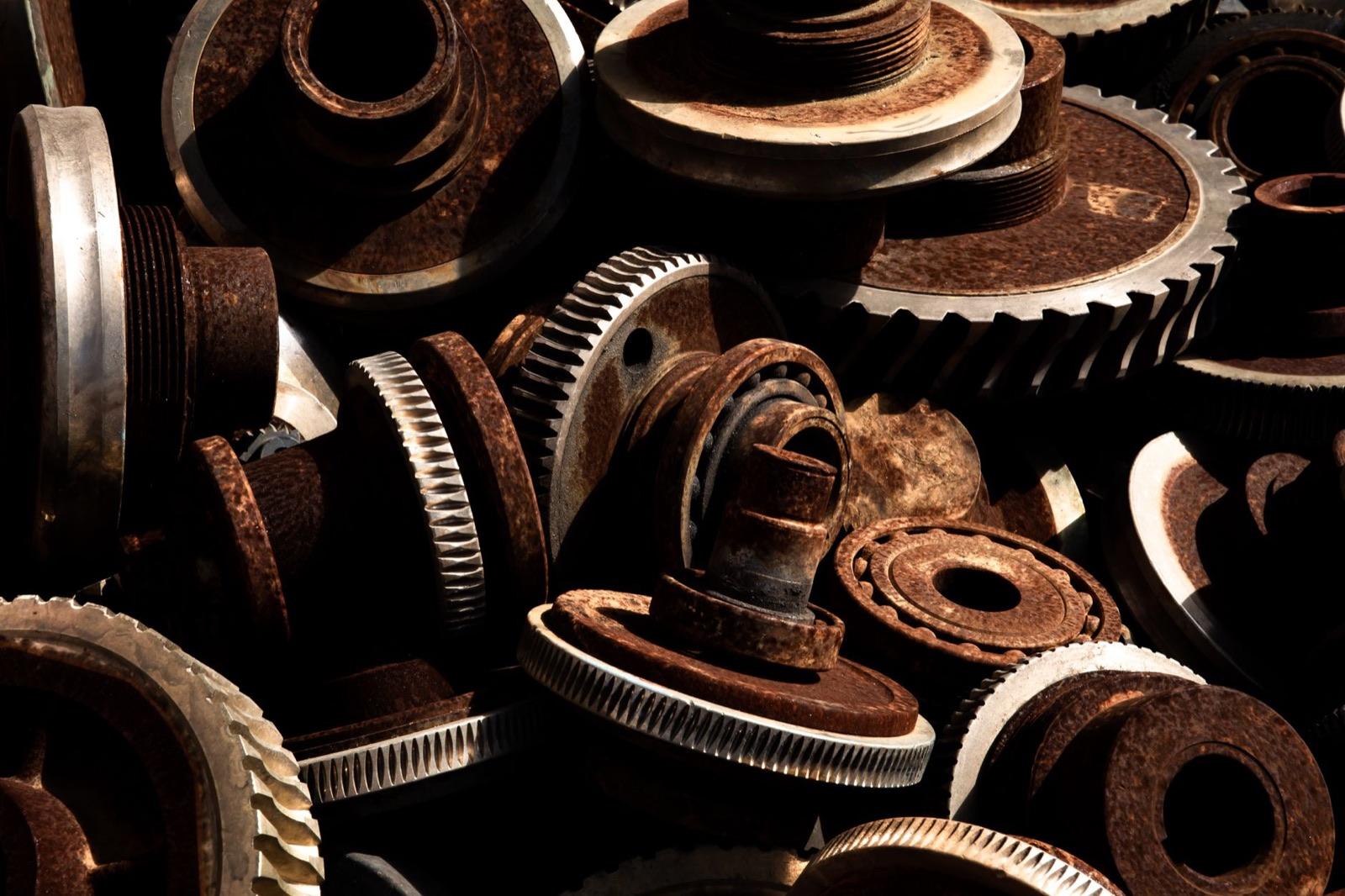 Pile of rusted, worn industrial gears and bearings — the aging mechanical components behind repeat elevator breakdowns