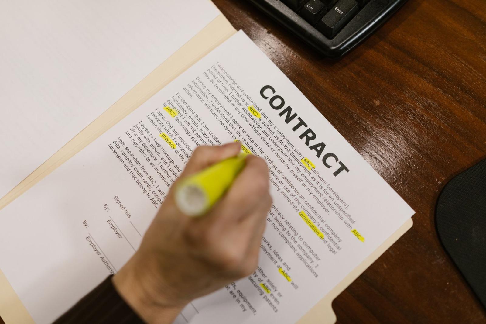 Hand marking clauses on a printed contract with a yellow highlighter at an office desk — reading the fine print of an elevator maintenance contract