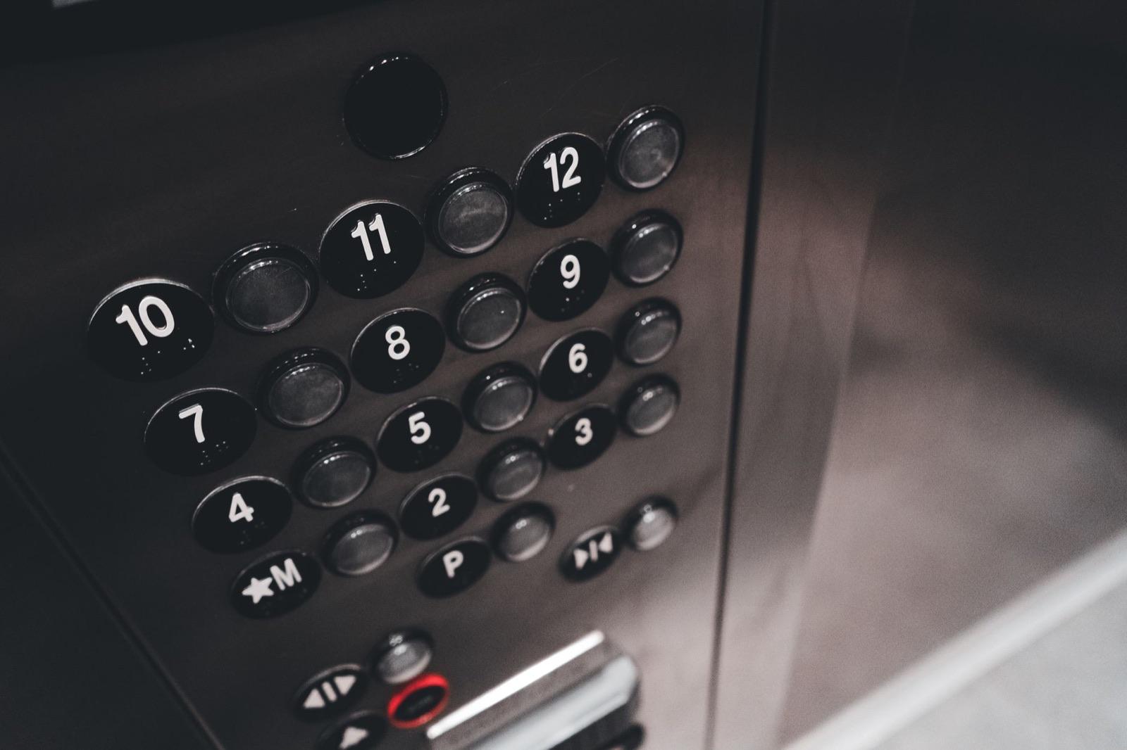 Metal elevator control panel with numbered buttons — in-car equipment governed by elevator code requirements